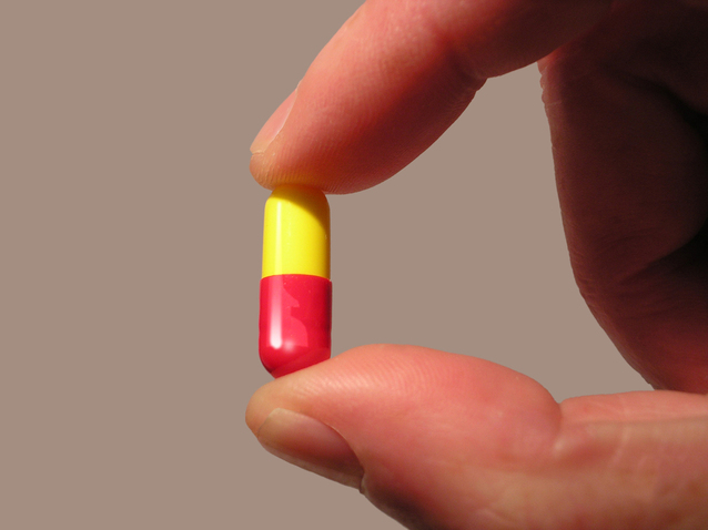 Človek drží medzi prstami žlto-ružovú tabletku